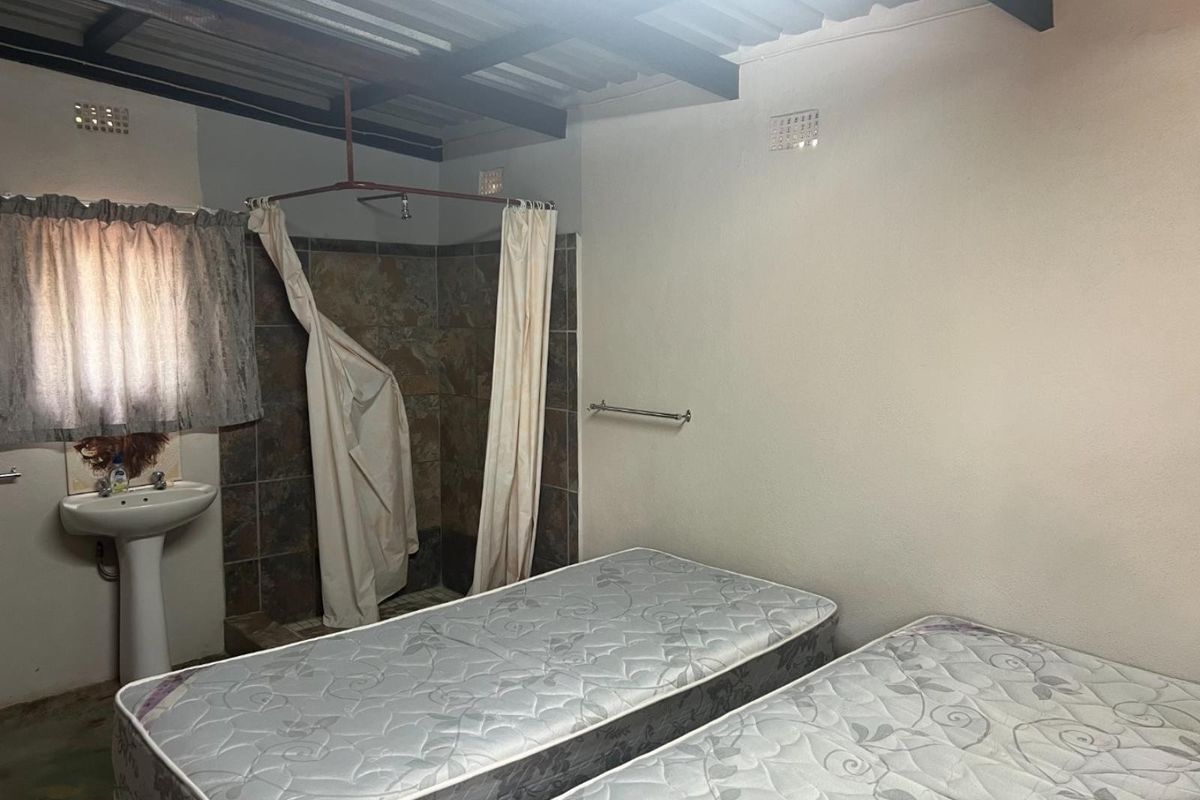 A functional bedroom featuring an integrated open-plan shower area with tiled surround and a pedestal basin.