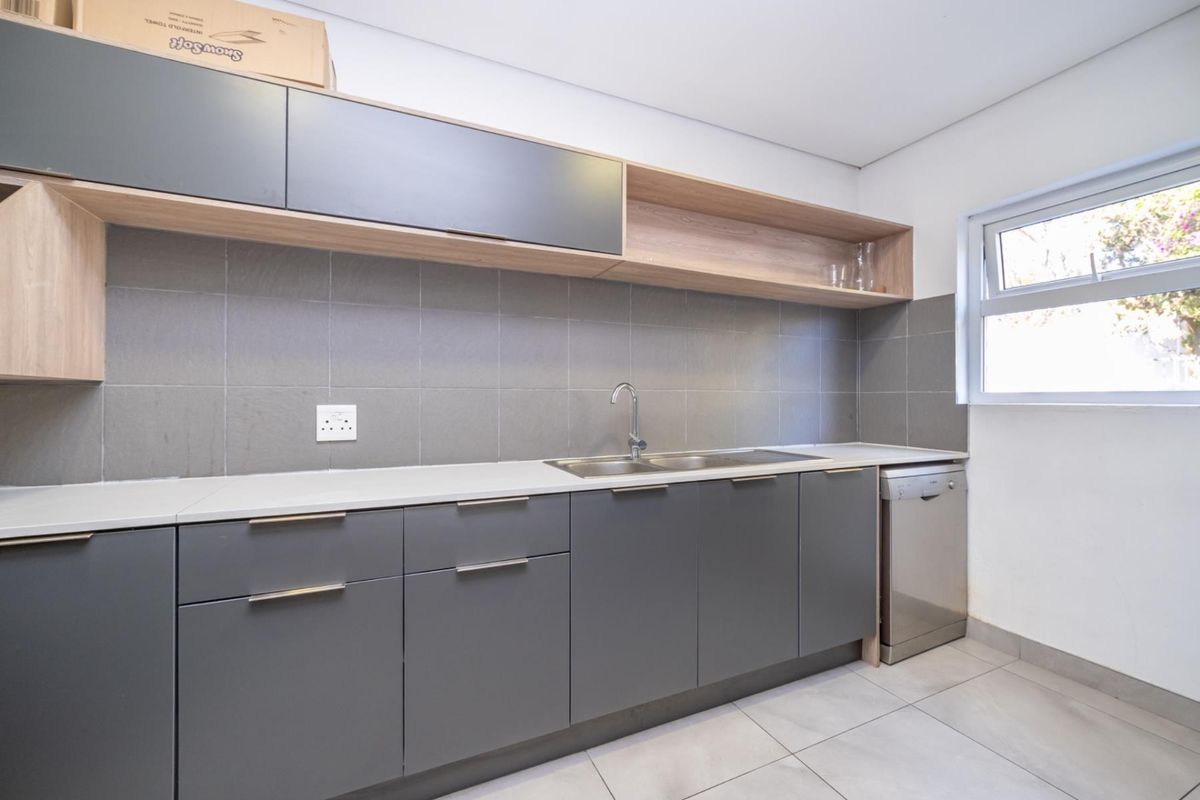 Modern kitchenette featuring sleek grey cabinetry, light wood open shelving, a stainless steel sink, and tiled backsplash in a clean, functional office space.