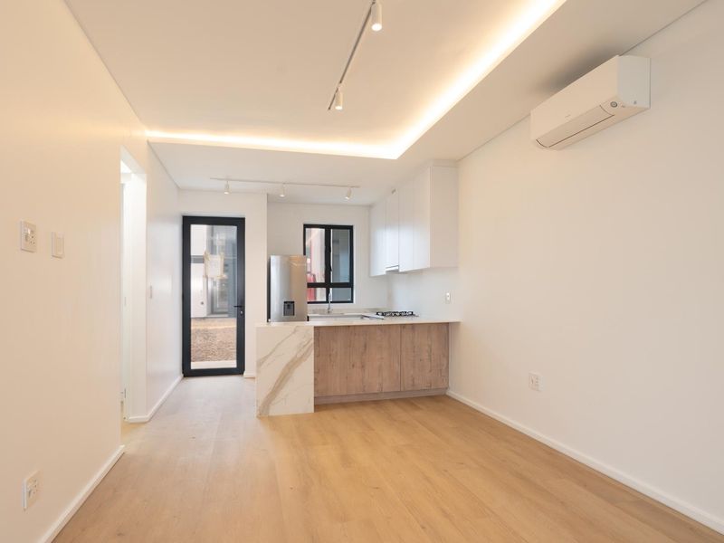 Modern open-plan kitchen and living area featuring sleek cabinetry, stone countertops, integrated appliances, recessed lighting, and split-system air conditioning in a bright, minimalist space.