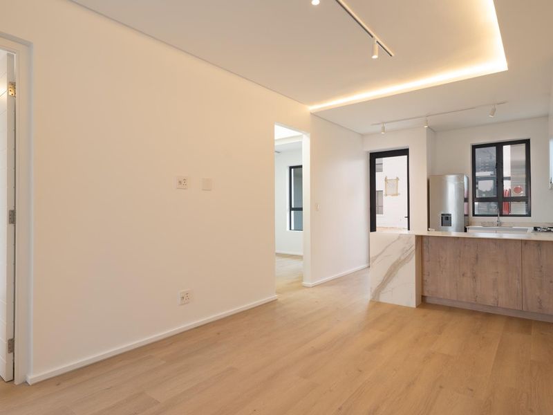 Modern open-plan living area featuring light laminate flooring, recessed ceiling lighting, and a contemporary kitchen with a stone-topped island.