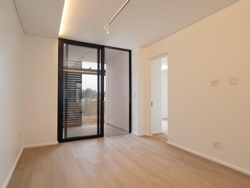 A bright, modern, and empty bedroom featuring light wood-look flooring, recessed ceiling lighting, and a large sliding glass door leading to an outdoor area.