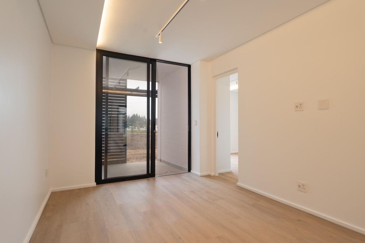 A bright, modern, and empty bedroom featuring light wood-look flooring, recessed ceiling lighting, and a large sliding glass door leading to an outdoor area.