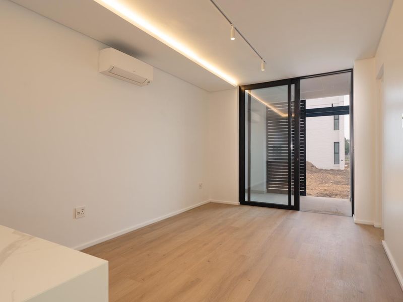 A bright, modern, and empty living area featuring laminate wood flooring, recessed strip lighting, a split-system air conditioner, and sliding glass doors to the exterior.