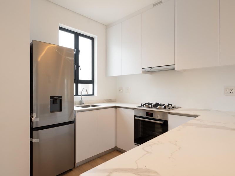 Modern kitchen featuring sleek white cabinetry, stone countertops, integrated gas hob, oven, and extractor fan, offering a clean and contemporary culinary space.