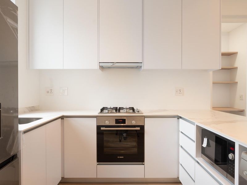 Modern kitchen featuring sleek white cabinetry, stone countertops, integrated appliances including a gas hob, oven, and microwave, with a clean, minimalist aesthetic.