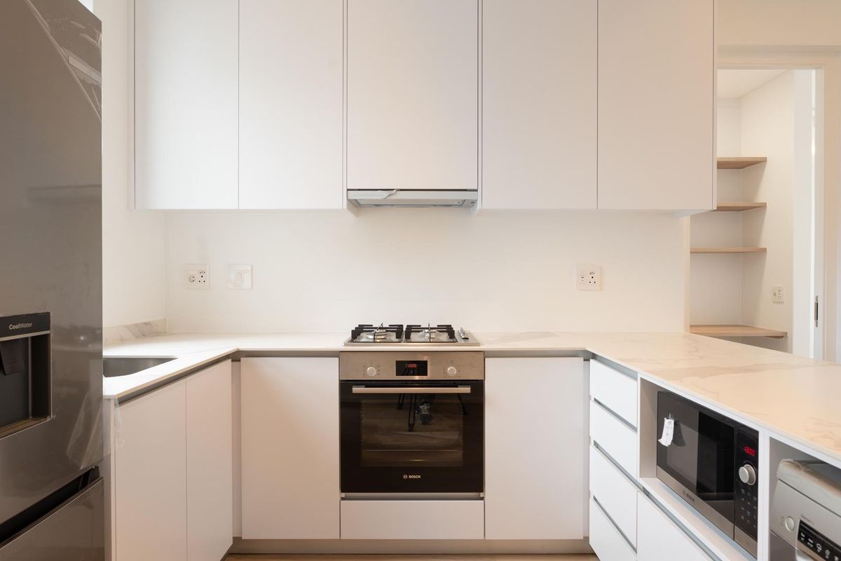 Modern kitchen featuring sleek white cabinetry, stone countertops, integrated appliances including a gas hob, oven, and microwave, with a clean, minimalist aesthetic.