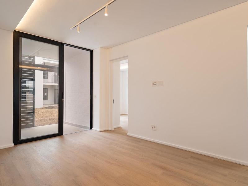 A bright, modern, and empty living area featuring light wood-look flooring, track lighting, and a large sliding glass door leading to an outdoor space.