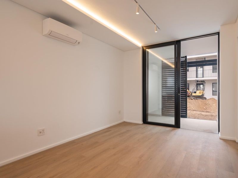 A bright, modern bedroom featuring timber laminate flooring, recessed lighting, a split-system air conditioner, and direct access to an outdoor patio area.