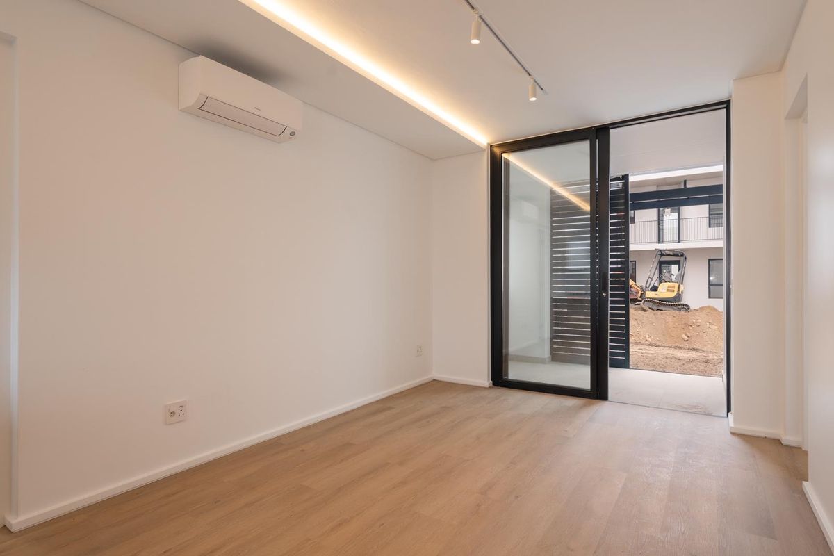 A bright, modern bedroom featuring timber laminate flooring, recessed lighting, a split-system air conditioner, and direct access to an outdoor patio area.
