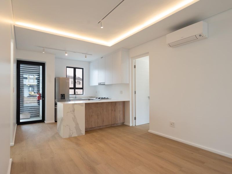 Modern open-plan kitchen and living area featuring sleek cabinetry, stone-topped breakfast bar, recessed lighting, and split-system air conditioning in a bright, neutral space.