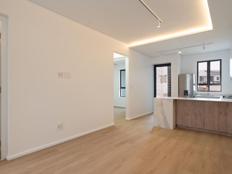 Modern open-plan living area featuring light laminate flooring, recessed ceiling lighting, and a contemporary kitchen with a stone-topped island and built-in cabinetry.