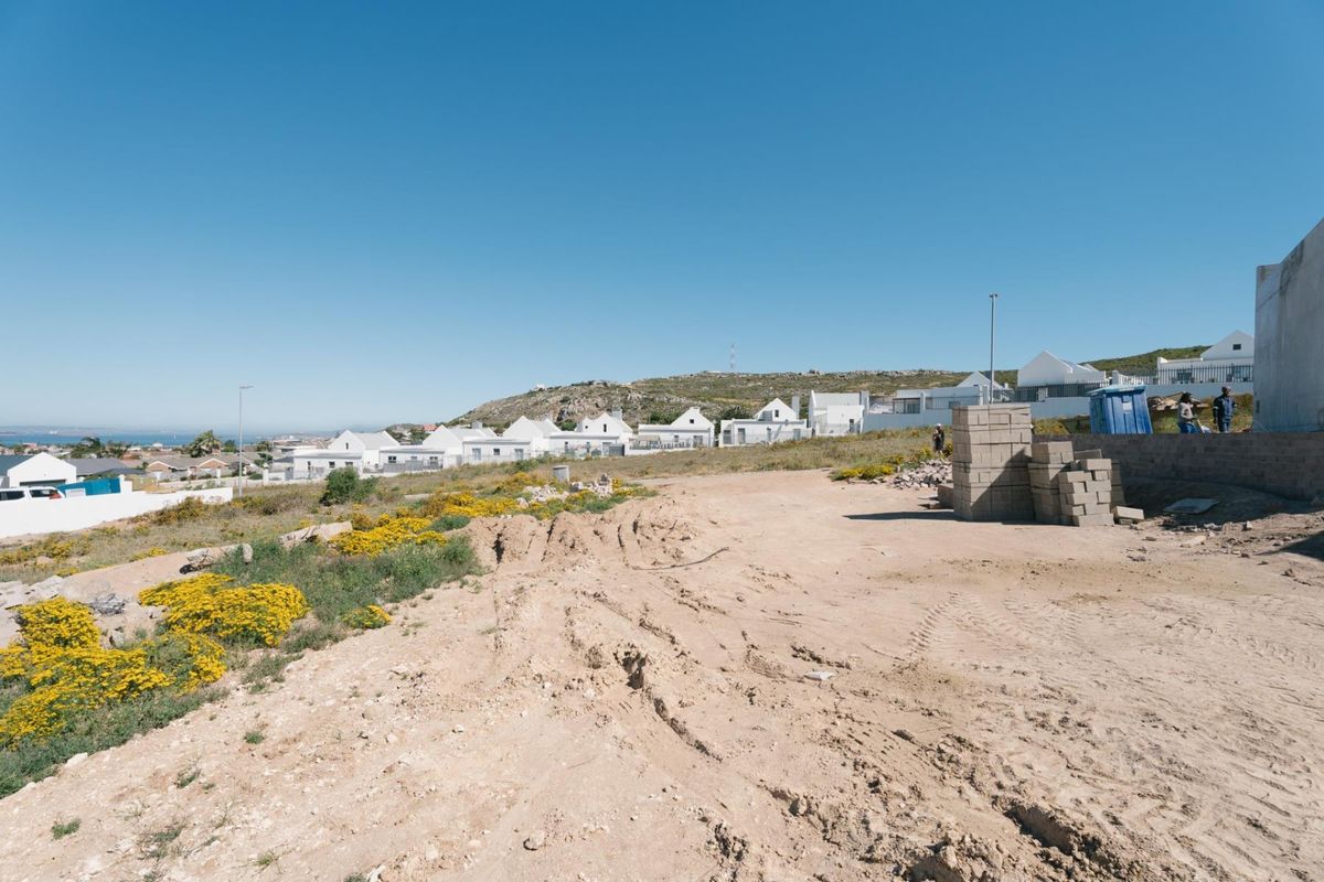 A vacant residential plot of land featuring a retaining wall and construction materials, situated in a developed coastal neighborhood.