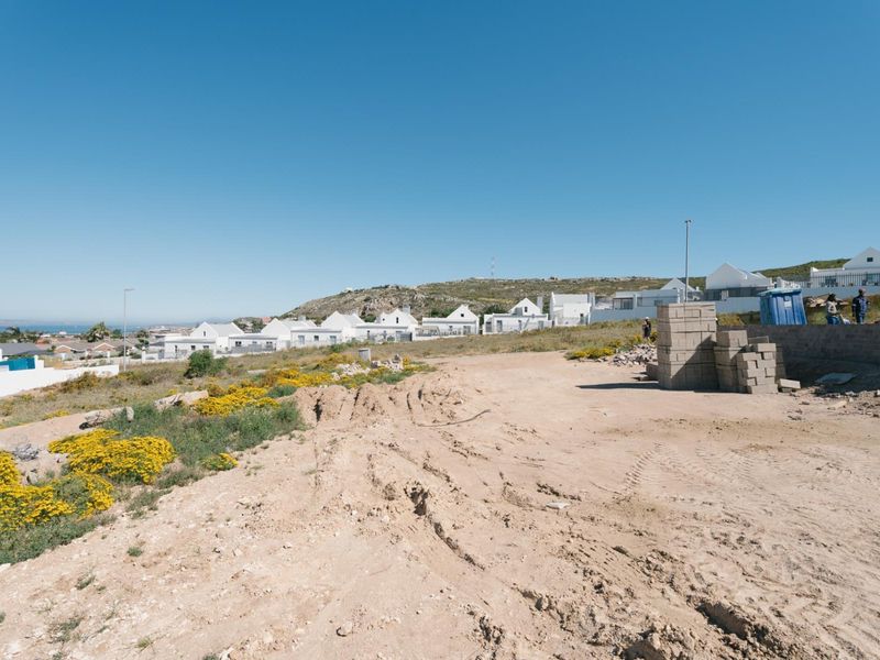 A vacant residential plot of land featuring a retaining wall and construction materials, situated in a developed coastal neighborhood.