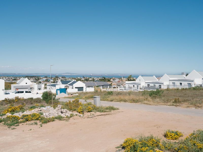 A wide-angle view of a residential neighborhood and distant coastline from a vacant plot of land.