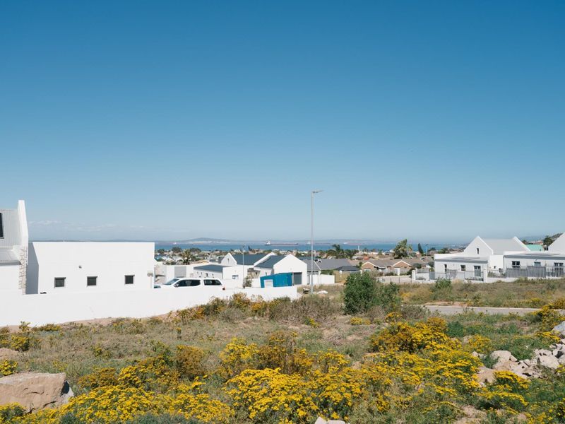 A scenic view overlooking a residential neighborhood with coastal landscape in the distance under a clear blue sky.