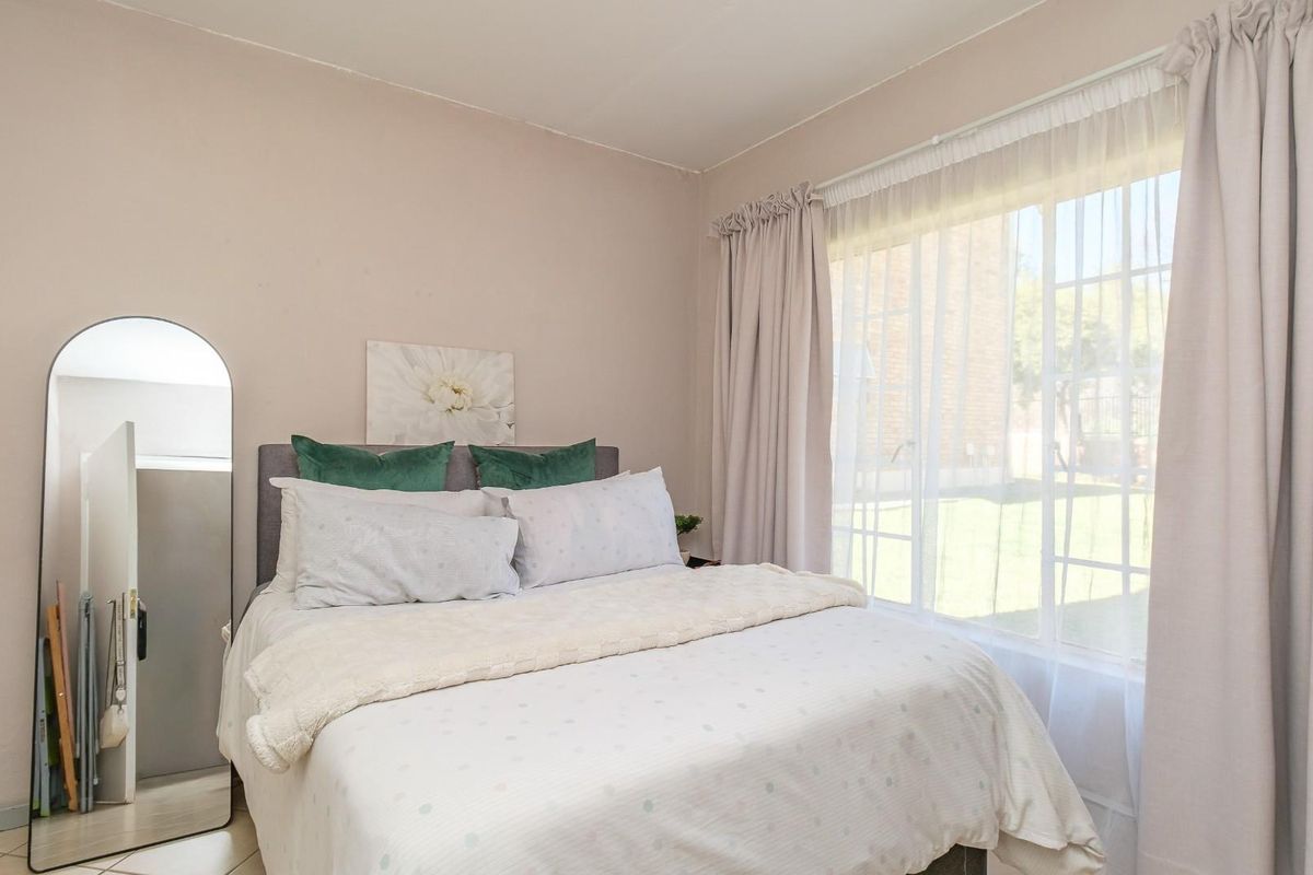 A bright bedroom featuring large windows with natural light, neutral wall tones, and tiled flooring, offering a comfortable and functional living space.