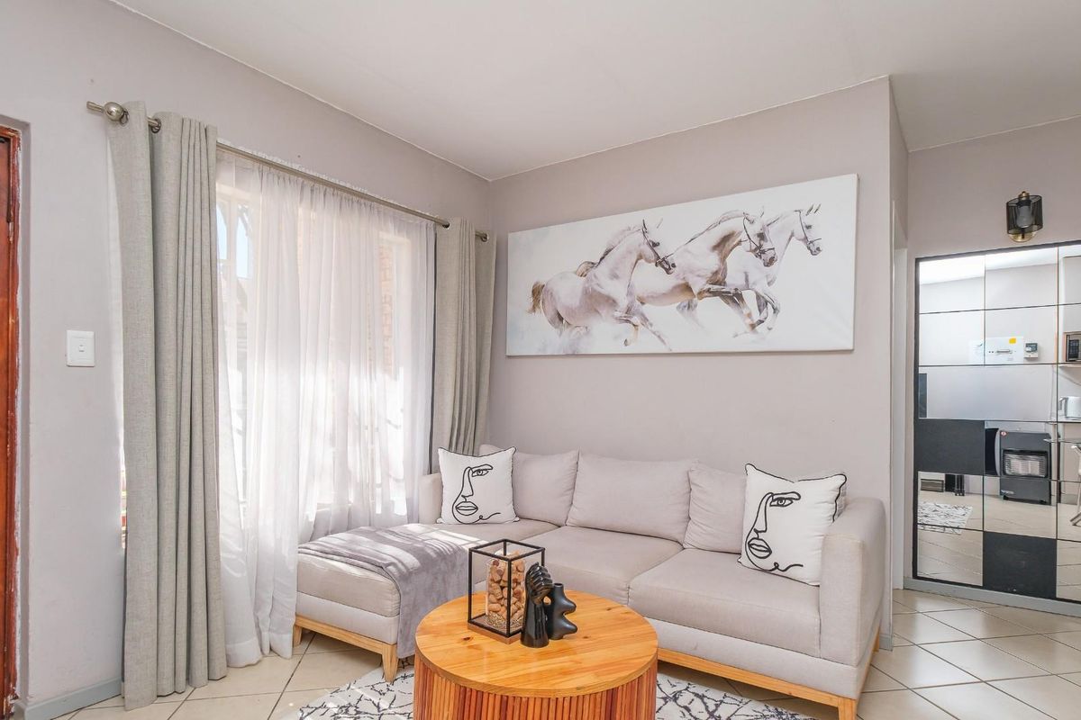 A cozy living room featuring tiled flooring, neutral wall tones, and a large window with curtain tracks, providing a bright and welcoming atmosphere.
