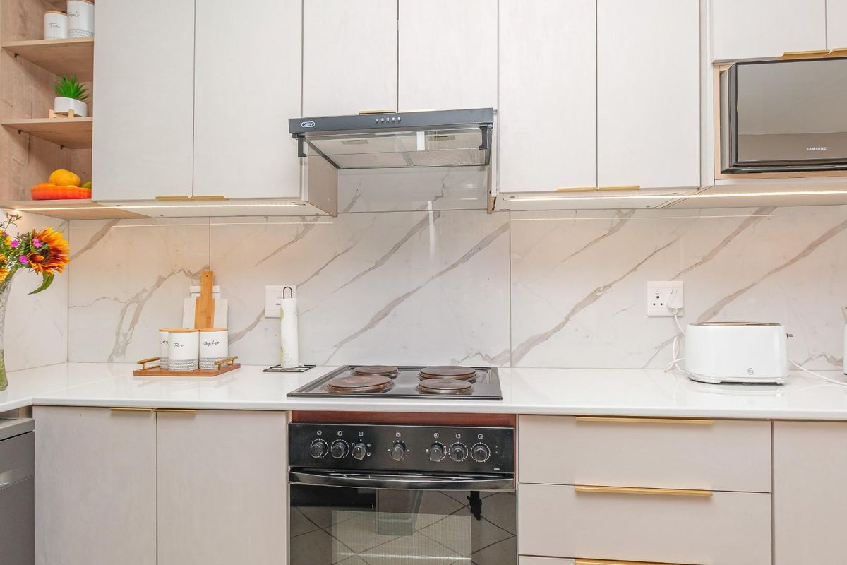 Modern kitchen featuring sleek cabinetry, marble-look splashback, built-in oven, electric hob, and integrated extractor fan with under-cabinet lighting.