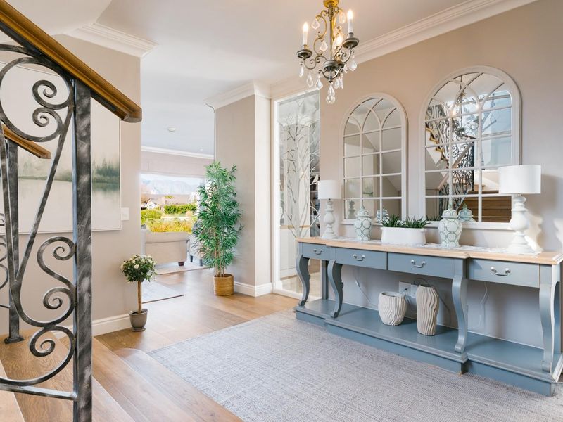 Elegant entrance hall featuring hardwood flooring, crown molding, a decorative wrought iron staircase railing, and a classic chandelier, leading into the main living area.