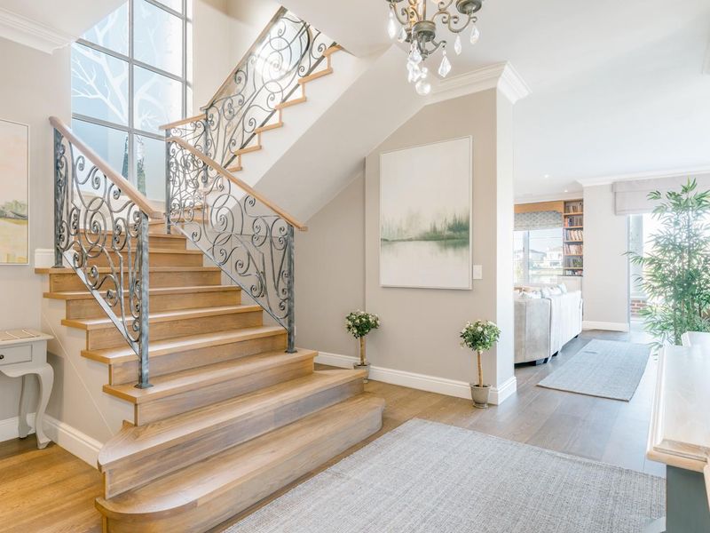 Elegant entrance hall featuring a grand timber staircase with ornate wrought iron balustrade, hardwood flooring, and sophisticated crown molding details.