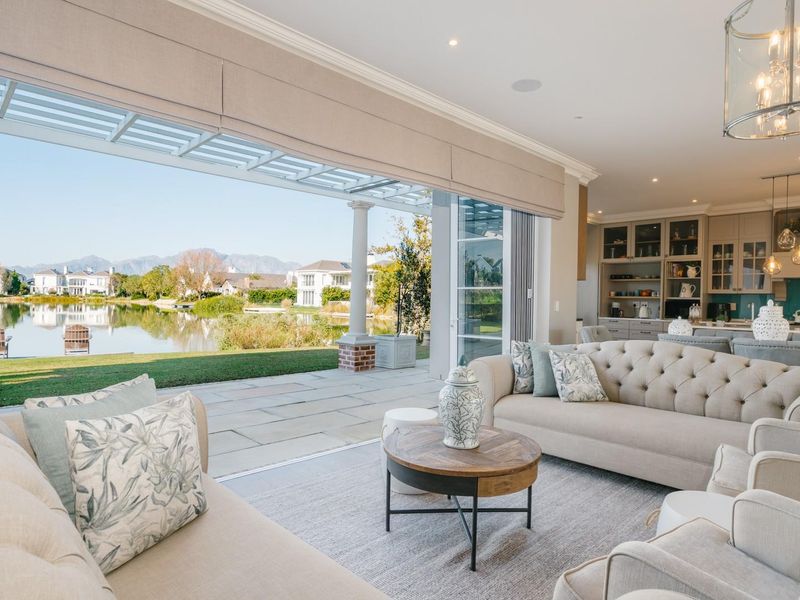 Spacious open-plan living area featuring seamless indoor-outdoor flow to a stone patio overlooking a scenic lake and mountain views.
