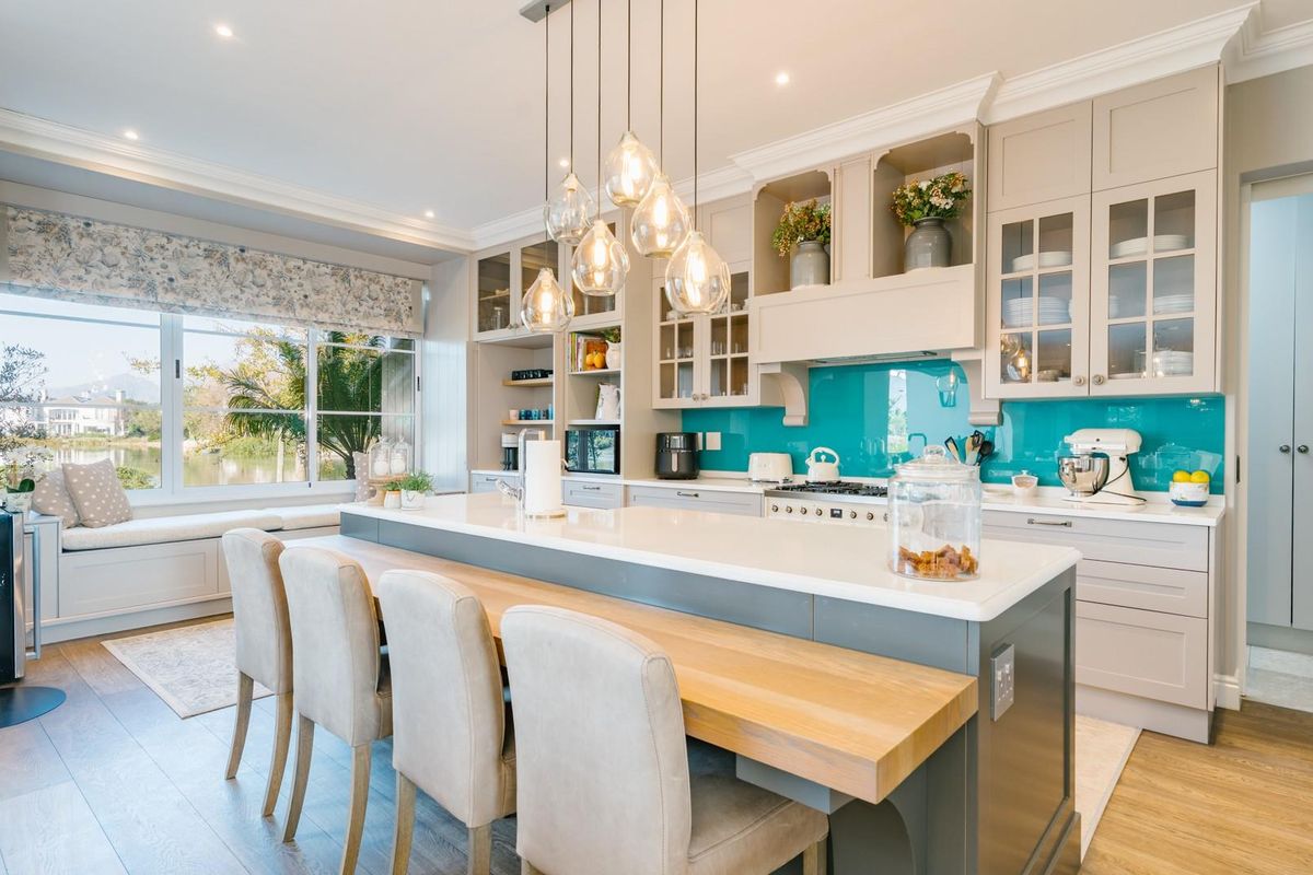Modern kitchen featuring a large central island with breakfast bar, quartz countertops, vibrant glass splashback, and custom cabinetry with integrated lighting.