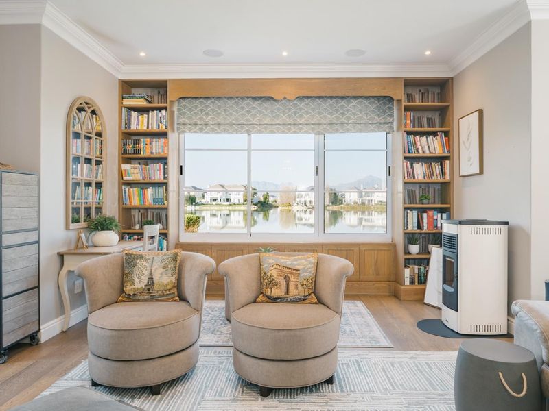 A well-appointed living room featuring custom built-in bookshelves, hardwood flooring, recessed lighting, and a pellet stove, with views overlooking the water.