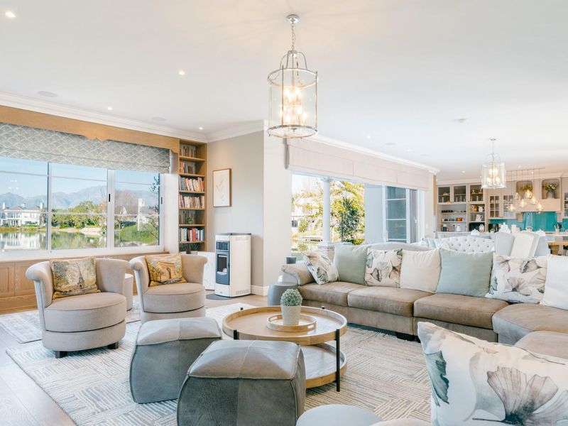 Spacious open-plan living area featuring built-in bookshelves, recessed lighting, and seamless flow into a modern kitchen with views of the surrounding landscape.