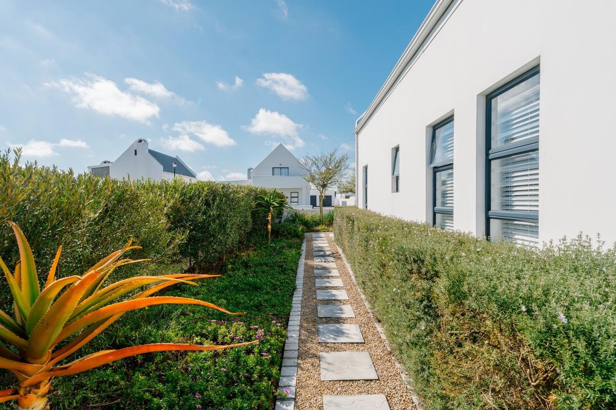 A well-maintained side garden path featuring stone pavers, gravel borders, and neatly trimmed hedges alongside the modern white exterior of the house.