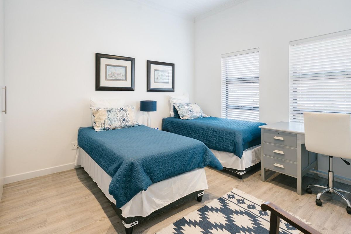 A bright and well-maintained bedroom featuring built-in cupboards and dual windows with fitted venetian blinds.