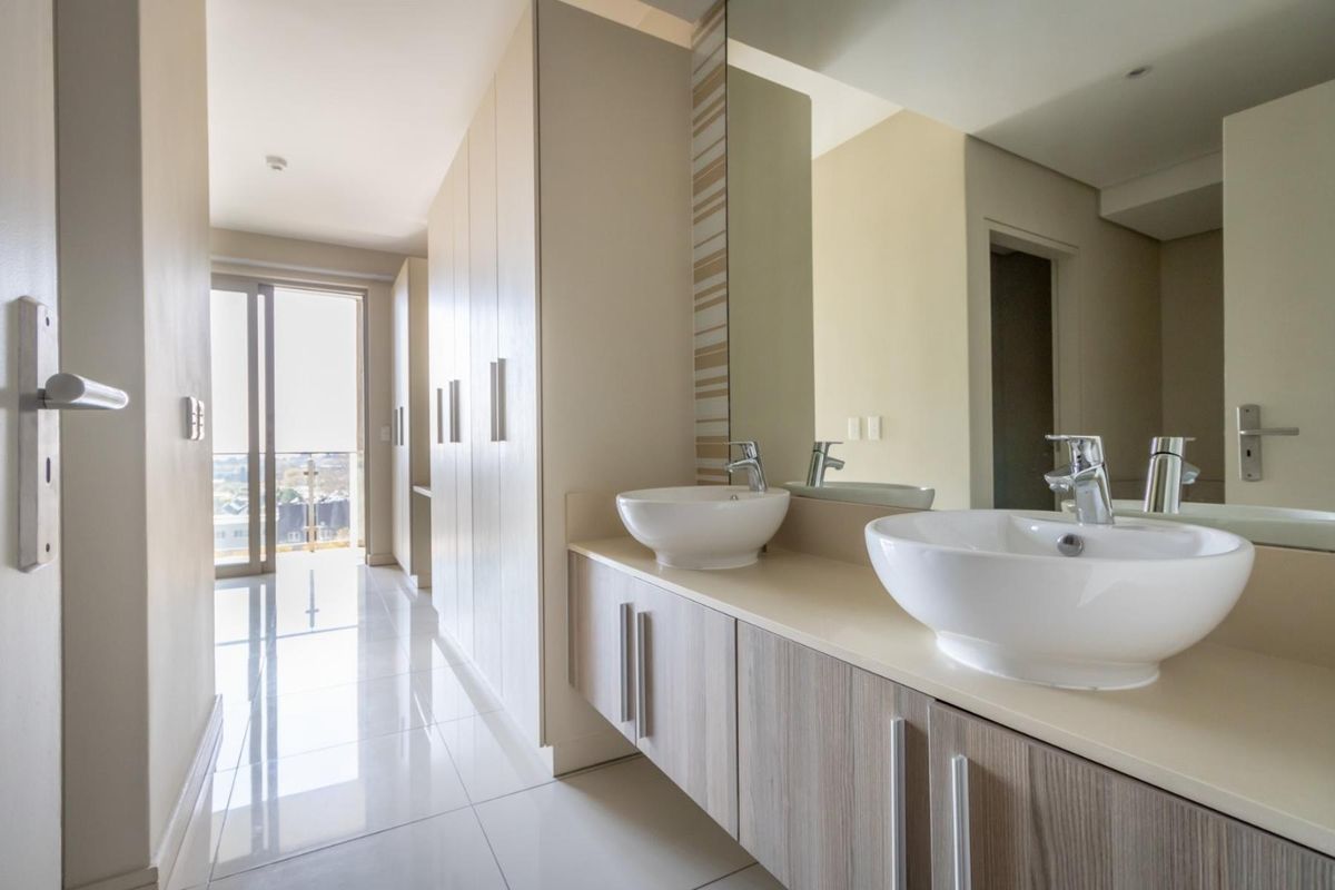 Modern bathroom featuring a double vanity with vessel sinks, sleek cabinetry, and large floor-to-ceiling built-in cupboards, leading to a balcony with city views.
