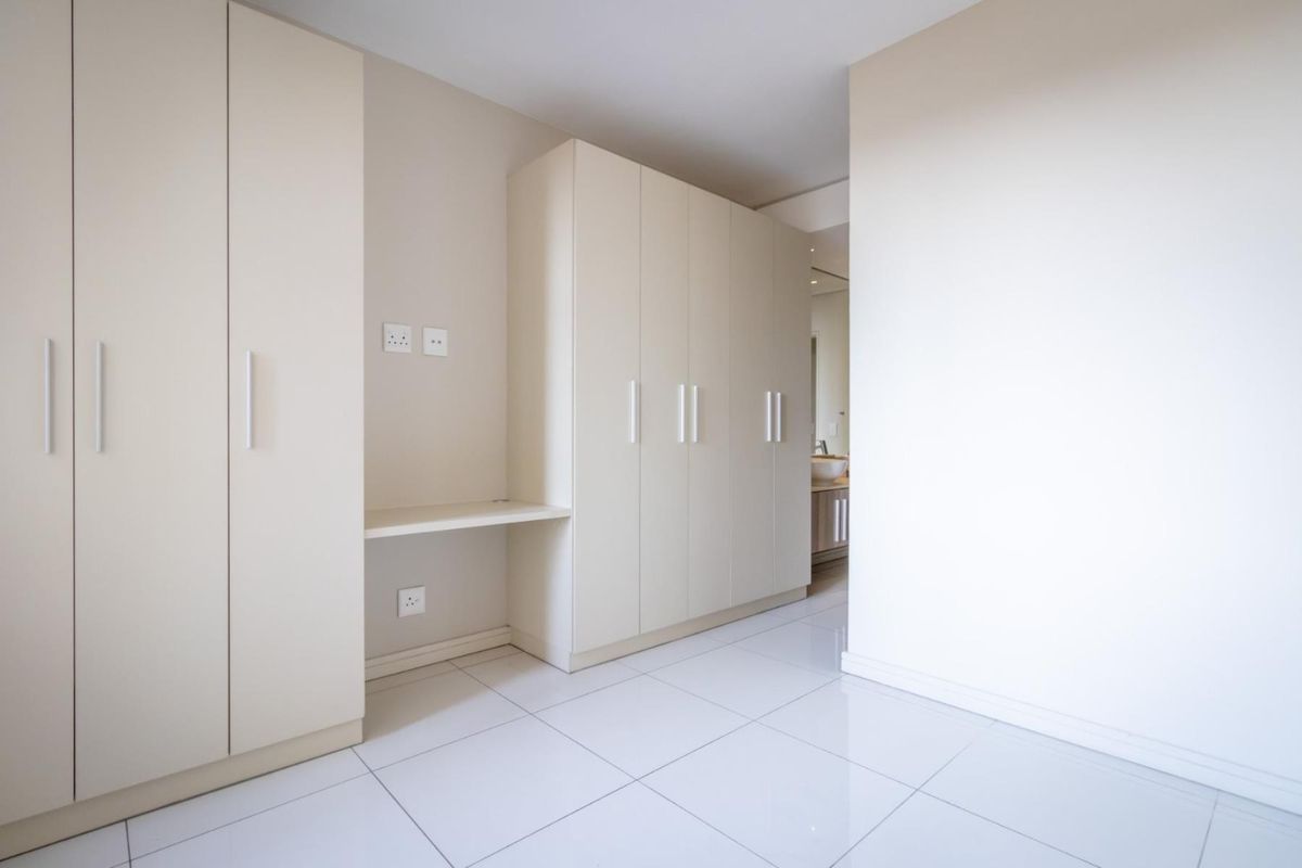A clean, modern bedroom featuring extensive built-in cabinetry with integrated desk space and polished tile flooring, leading into an adjacent bathroom area.