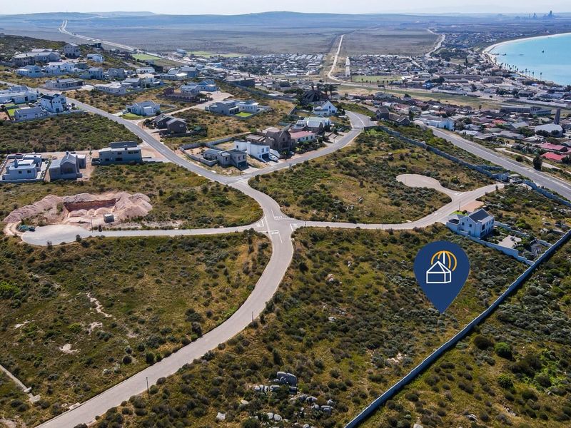 Aerial view of a vacant residential plot situated in a coastal estate, featuring established road access and proximity to the ocean.