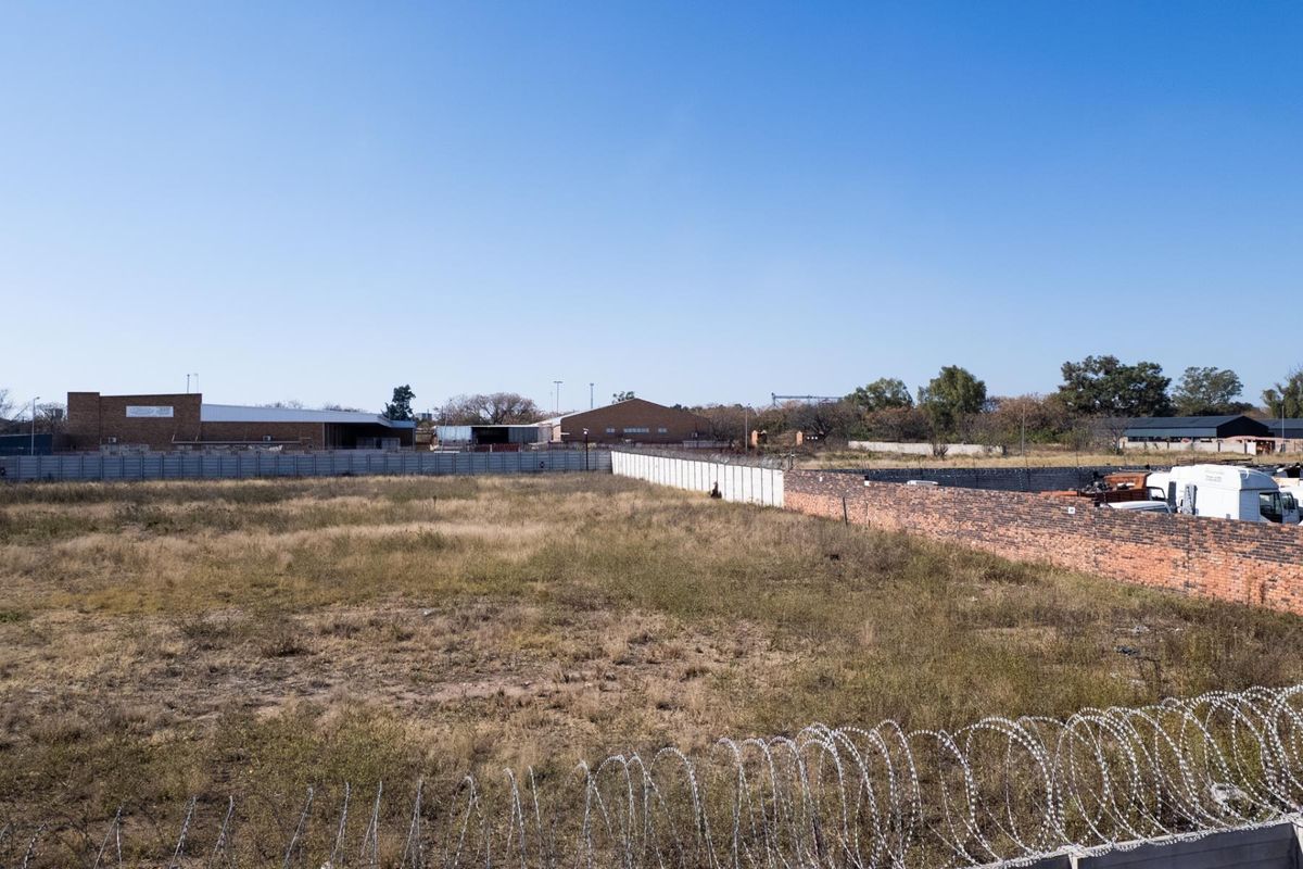 A vacant agricultural land plot enclosed by precast concrete and brick boundary walls with razor wire security fencing.