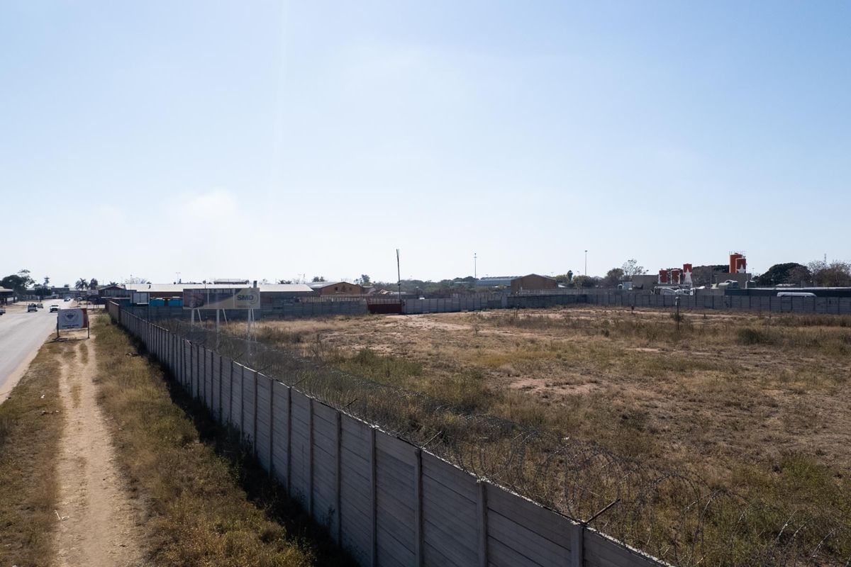 A vacant agricultural land plot enclosed by a precast concrete wall with security razor wire, situated along a roadside.