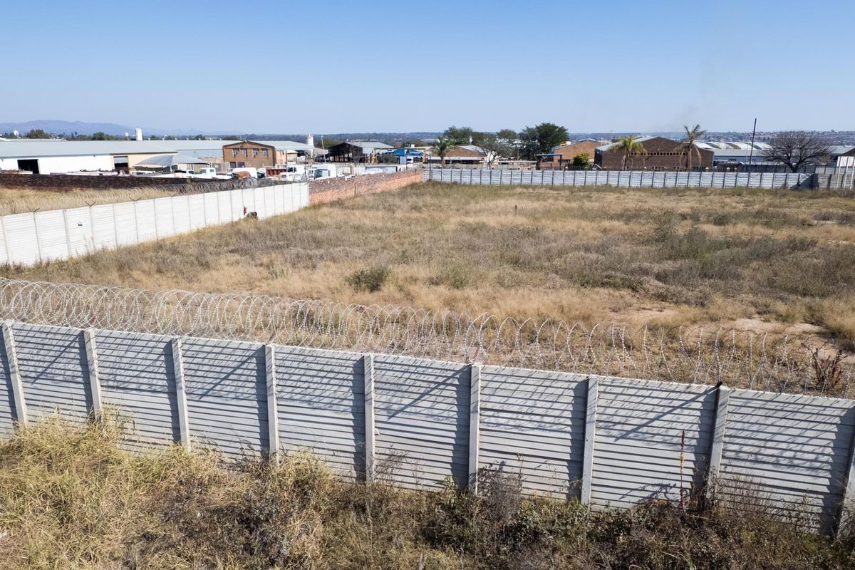 An elevated view of a vacant agricultural plot enclosed by precast concrete perimeter walls topped with razor wire security fencing.