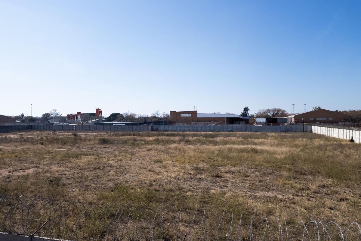 A vacant agricultural land plot enclosed by a precast concrete boundary wall with razor wire security fencing.