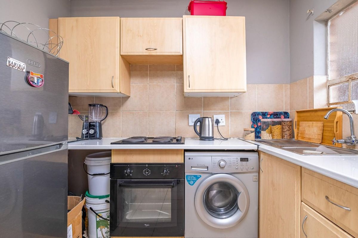 Compact kitchen featuring light wood cabinetry, tiled backsplash, built-in oven, electric hob, and integrated laundry appliance space.