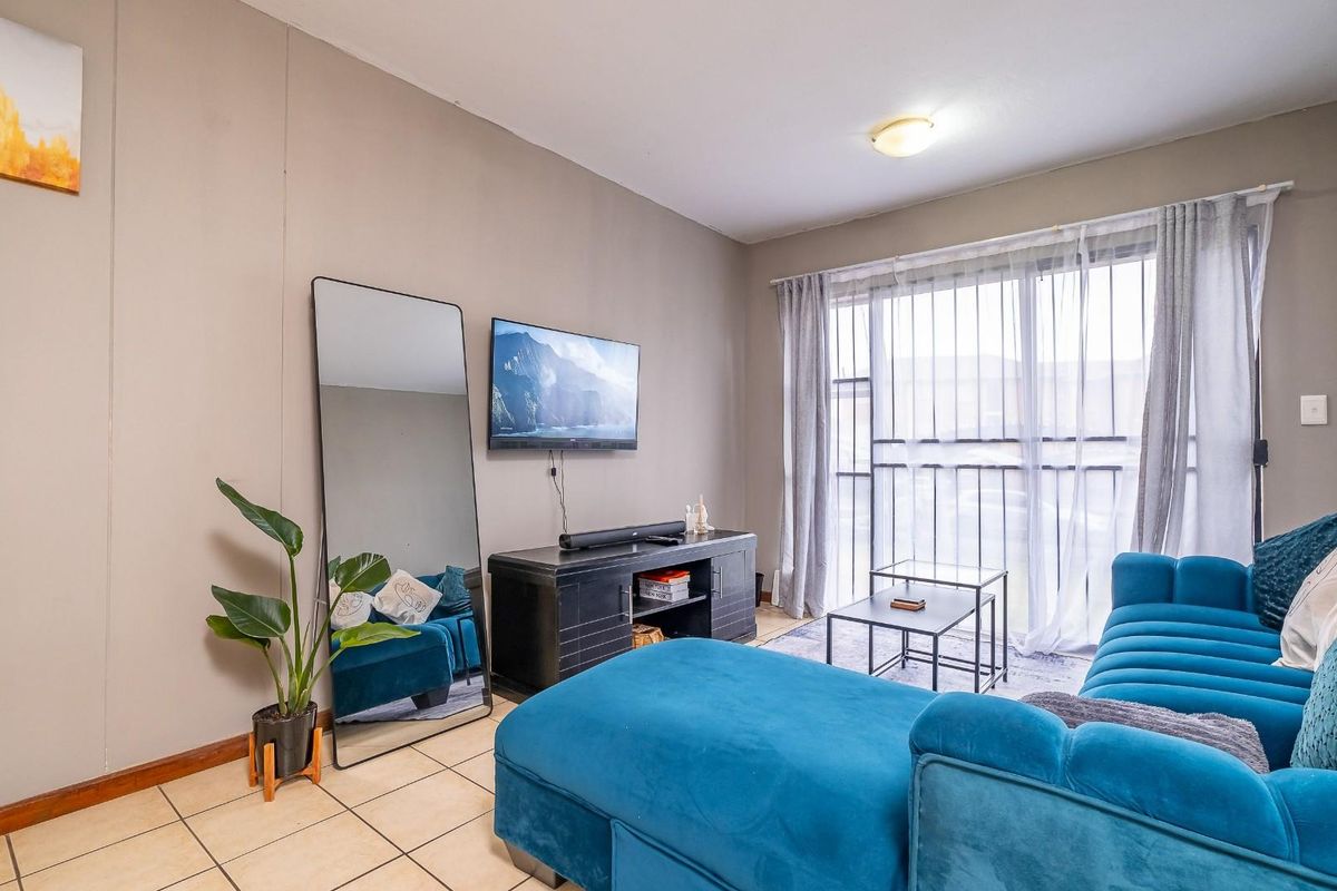 A living room featuring tiled flooring and a large sliding glass door with an integrated security gate, providing access to the exterior.
