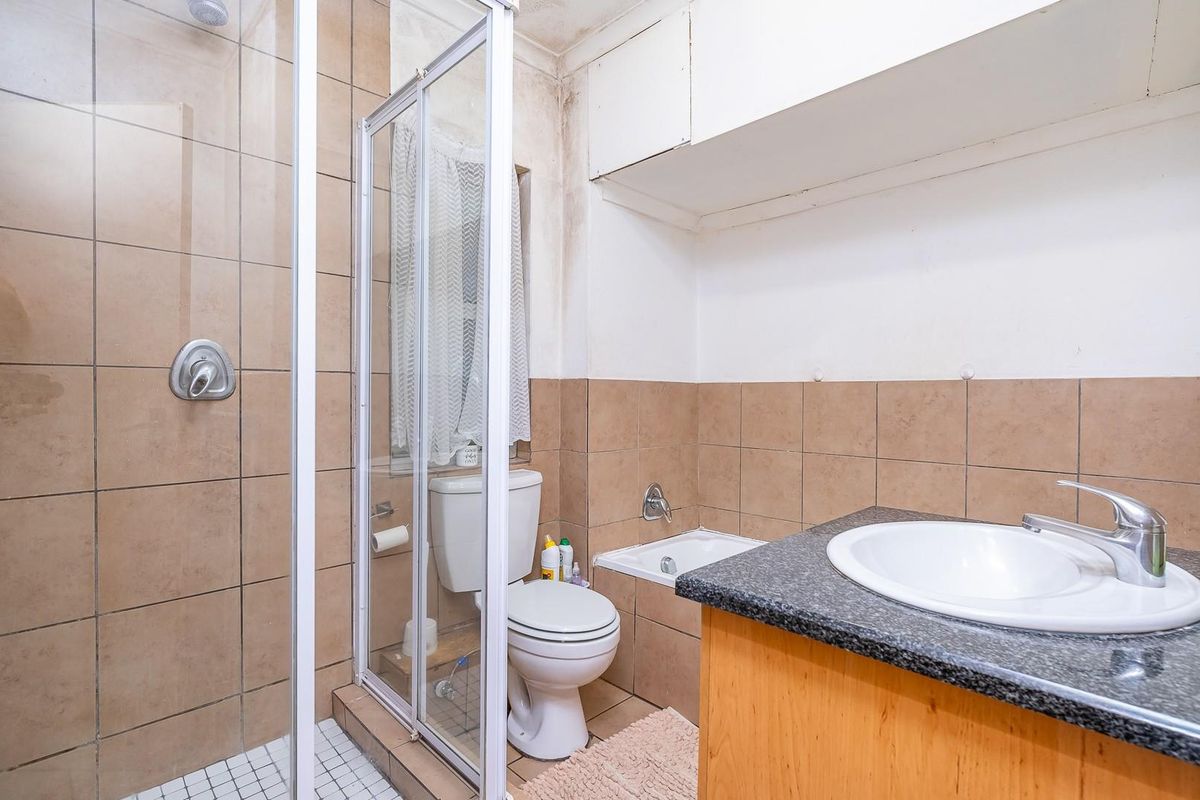 A functional bathroom featuring a shower enclosure, vanity with granite countertop, and built-in storage, currently showing signs of wear and ceiling water damage.