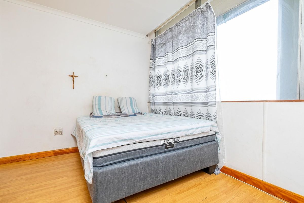 A functional bedroom featuring laminate flooring, a built-in wardrobe, and a large window providing natural light.