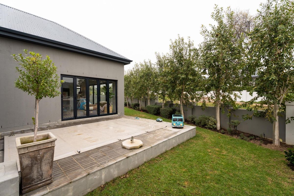 Rear exterior view featuring a concrete patio with a swimming pool cover, bi-fold doors leading to the interior, and a well-maintained garden.