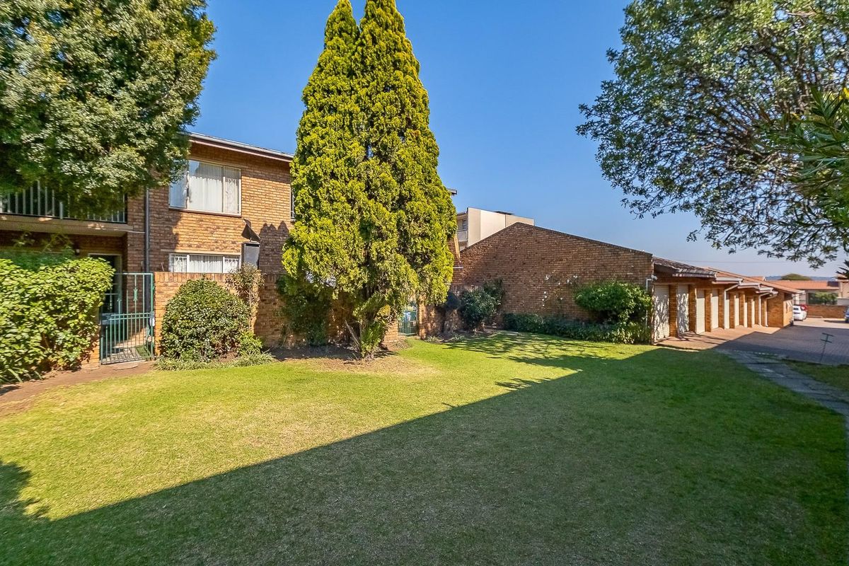 A view of the rear exterior of the apartment complex, featuring a shared lawn, brick building facade, and a row of garages.