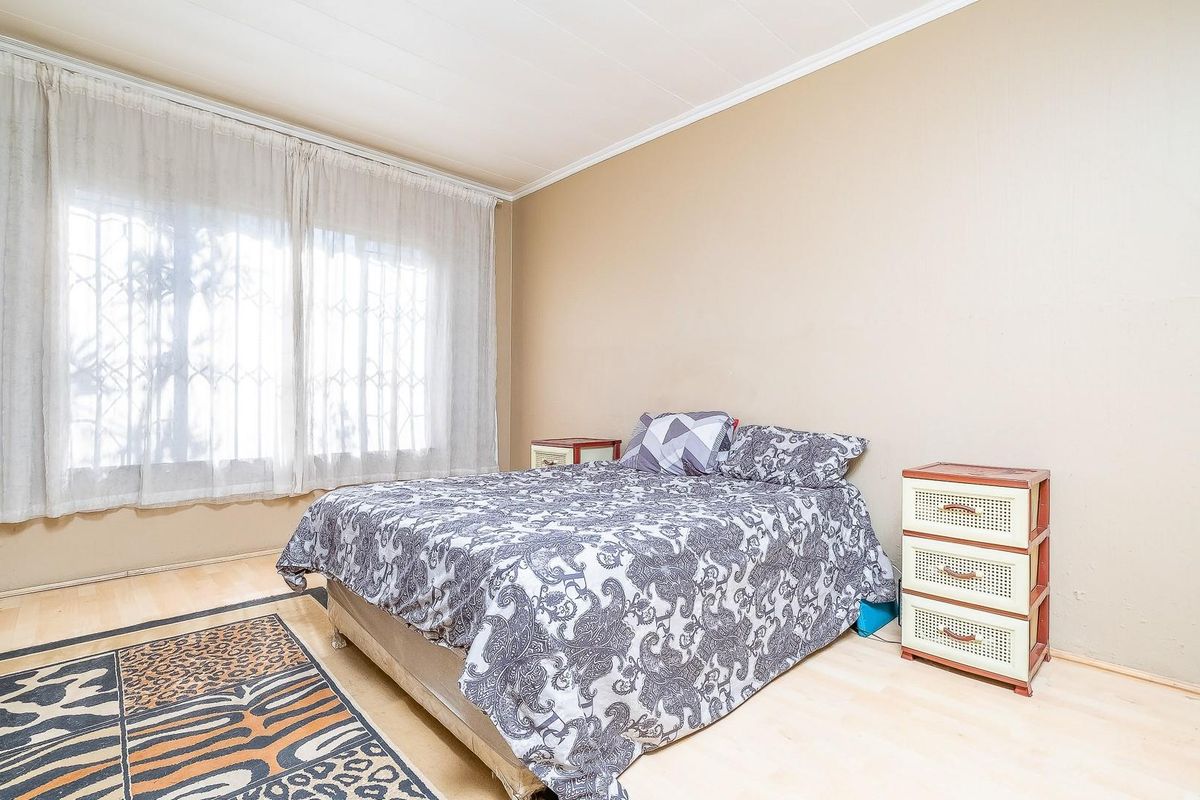 A standard bedroom featuring light-toned laminate flooring and a large window fitted with a security gate.