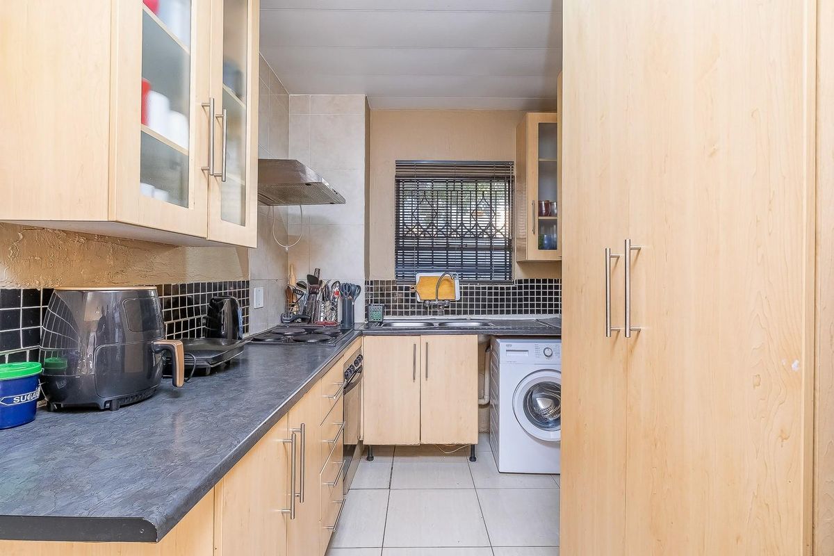 Functional kitchen featuring light wood cabinetry, dark laminate countertops, tiled backsplash, built-in cooking appliances, and a dedicated space for a washing machine.