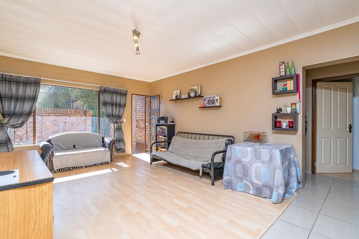 A spacious living area featuring laminate flooring, a large window providing natural light, and a neutral wall finish, offering a versatile space for relaxation.