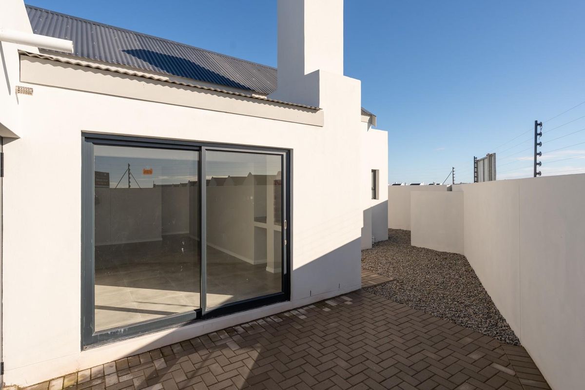 A clean rear exterior view featuring a paved patio, gravel garden area, and a modern sliding glass door leading into the home.
