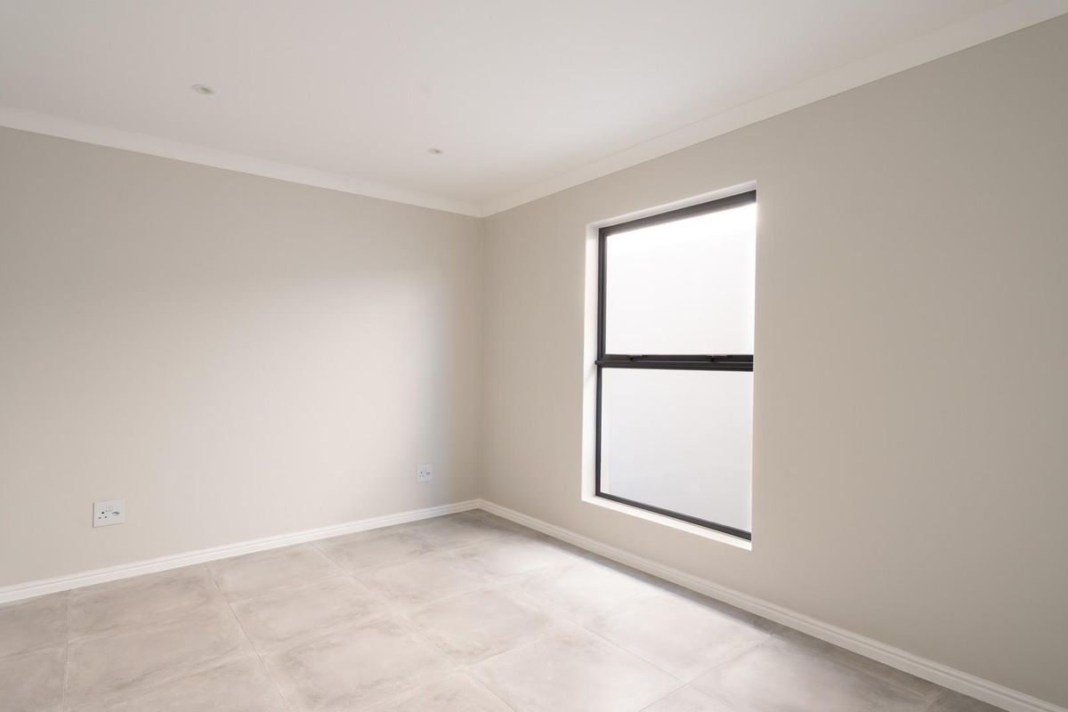 A bright, neutral-toned bedroom featuring modern tiled flooring, recessed lighting, and a sleek black-framed window, offering a clean and versatile living space.