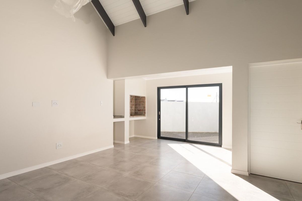 Spacious living area featuring a vaulted ceiling with exposed beams, tiled flooring, and a built-in braai, leading out to an outdoor space.