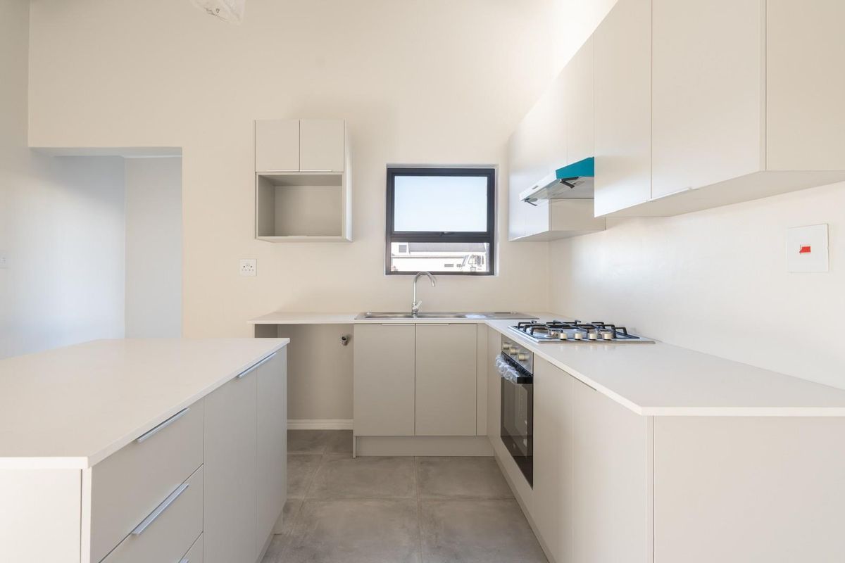 Modern, minimalist kitchen featuring neutral cabinetry, stone countertops, a central island, and integrated gas cooking appliances in a clean, open-plan layout.
